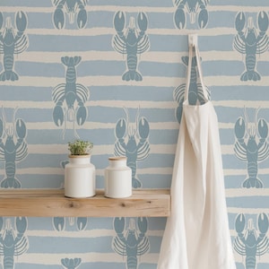 May include: Wallpaper featuring a repeating pattern of blue lobsters on a background of horizontal light blue and white stripes. A wooden shelf holds two white canisters, and a white apron hangs from a hook on the wall.