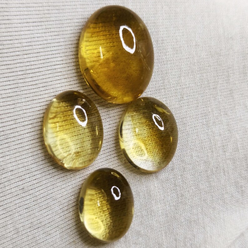May include: Four oval-shaped, golden-yellow gemstones. The stones vary in size, with one larger stone at the top and three smaller stones arranged below. Each stone has a polished, translucent appearance, reflecting light.