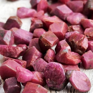 Peut inclure: Une collection de rubis bruts et non polis dans diverses nuances de rose profond et de rouge. Ces pierres naturelles présentent des formes irrégulières et facettées avec une texture mate à semi-translucide, révélant leur structure cristalline brute.