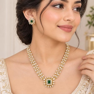 Puede incluir: Un collar de varias hebras con tres filas de pequeñas perlas blancas y un colgante cuadrado central con una piedra verde rodeada de cristales transparentes y perlas. Los pendientes cuadrados a juego presentan una piedra verde central.