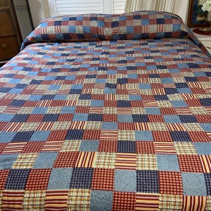 May include: A patchwork quilt with a repeating pattern of red, white, and blue squares and rectangles. The quilt is on a bed with a matching pillow. The quilt's design includes stripes, checks, and solid colors.
