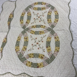 May include: Cream-colored quilt with a double wedding ring design. The rings are made of floral and solid fabric in shades of green, yellow, and red. The quilt has a scalloped edge with a green trim.