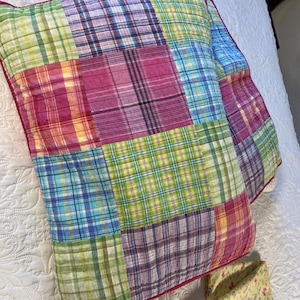 May include: A rectangular quilted pillow sham featuring a patchwork design of various plaid patterns in shades of pink, purple, blue, yellow, and green. The sham is finished with a dark pink piped edge and has a stitched grid texture.