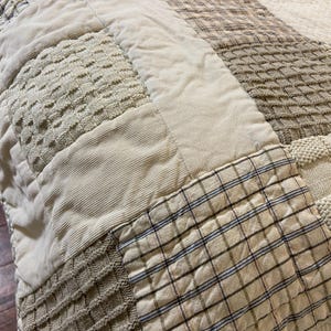 May include: Close-up of a patchwork quilt in neutral tones. The quilt features various textures, including corduroy, woven, and plaid fabrics. The color palette consists of beige, cream, and light brown hues, creating a cozy and inviting aesthetic.