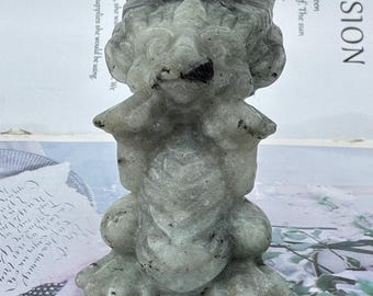 May include: A carved stone figurine of a mythical creature, possibly a griffin or dragon, in shades of gray and white. The sculpture has detailed features, including a head with a mane, wings, and a body with clawed feet. The background is blurred.