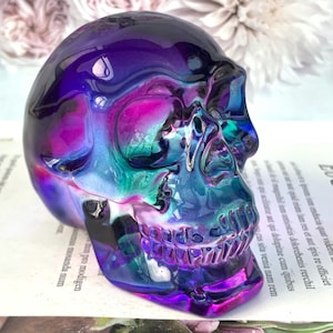 May include: A decorative skull sculpture in iridescent colors. The skull is a mix of purple, blue, and pink hues, with a glossy finish. The sculpture is a unique piece of home decor.