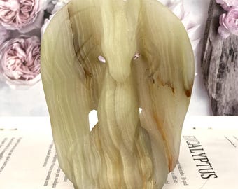 May include: A carved stone sculpture of a bird or angel with outstretched wings. The sculpture is made of a light green and brown stone, with a smooth, polished surface. The sculpture has a unique, abstract design.