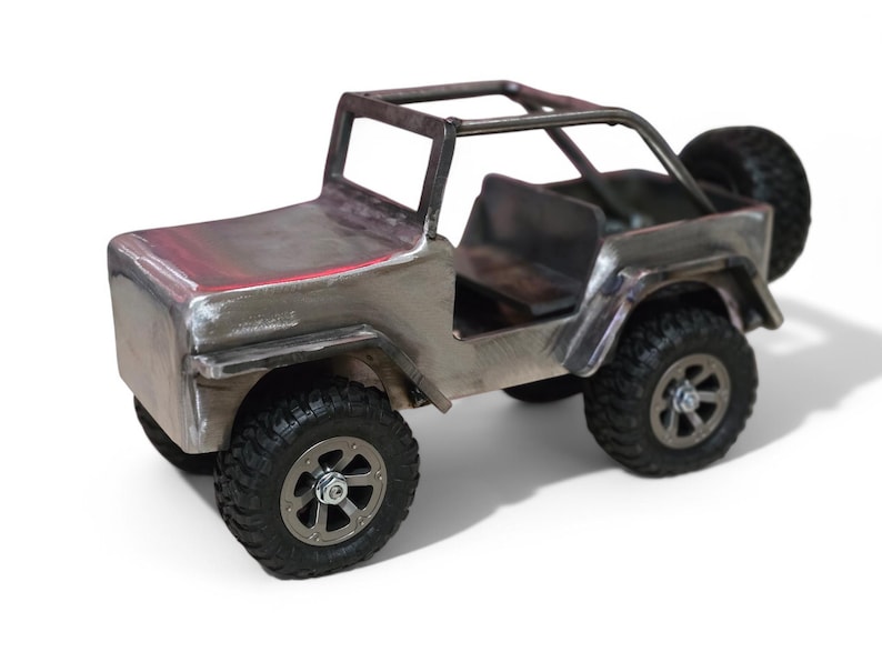 K&ouml;nnte beinhalten: Ein handgefertigter Metall-Spielzeug-Jeep mit &Uuml;berrollk&auml;fig und Ersatzreifen. Der silberfarbene Jeep hat schwarze Reifen und einen detaillierten Innenraum. Der Spielzeug-Jeep ist eine Miniatur-Nachbildung eines klassischen Gel&auml;ndewagens.