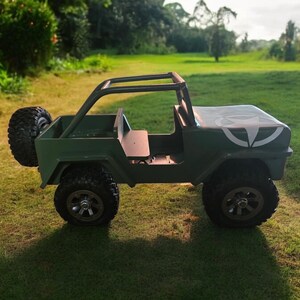 K&ouml;nnte beinhalten: Ein gr&uuml;ner Spielzeug-Jeep mit schwarzen Reifen und einem &Uuml;berrollb&uuml;gel. Der Jeep hat ein Ersatzrad hinten und eine wei&szlig;e Grafik auf der Motorhaube. Der Jeep steht auf einer Wiese.