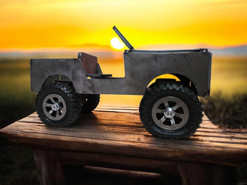 K&ouml;nnte beinhalten: Ein handgefertigtes Metall-Spielzeug-Jeep mit gro&szlig;en, robusten Reifen und einem braunen Sitz. Der Jeep hat eine Windschutzscheibe und einen &Uuml;berrollb&uuml;gel. Das Spielzeug steht auf einem Holztisch mit Sonnenuntergang im Hintergrund.
