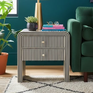 May include: A living room scene featuring a green sofa, a black and white striped nightstand, and a white lamp with a gold base. A potted plant and a patterned rug complete the decor. A painting hangs on the teal wall.