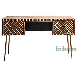 May include: A wooden desk with a geometric pattern in shades of brown and tan. The desk has two drawers with brass-colored handles and slender, gold-colored legs. The desk has a black interior and the text "En deore." is visible.