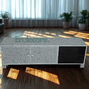 Op de afbeelding: Een rechthoekige kast met een wit en zwart geometrisch patroon. Het heeft twee deuren en een open plank. De kast staat op een houten vloer. De kamer heeft grote ramen en potplanten.