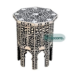 May include: Black and white octagonal side table with floral inlay design. The table features a detailed pattern on the top and sides, with arched cutouts at the base. A decorative accent piece for any room.