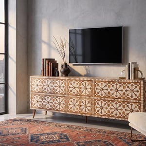 Könnte beinhalten: Ein TV-Schrank aus Holz mit geometrischem Muster, gekrönt von Büchern, einer Vase und einem Fernseher. Der Schrank hat sechs Schubladen mit einem sich wiederholenden Sternmuster in Weiß und Braun. Ein gemusterter Teppich und ein großes Fenster sind im Hintergrund.