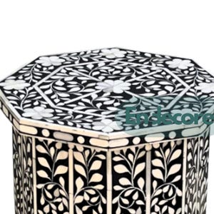 May include: Black and white octagonal side table with floral inlay design. The table features a detailed pattern of white flowers and leaves against a black background. The table's design is symmetrical and decorative.