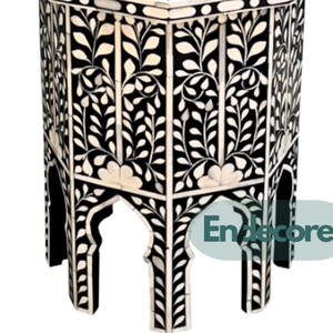 May include: A black and white hexagonal side table with a floral design. The table features a repeating pattern of white floral and leaf motifs against a black background. The table's legs have an arched design.