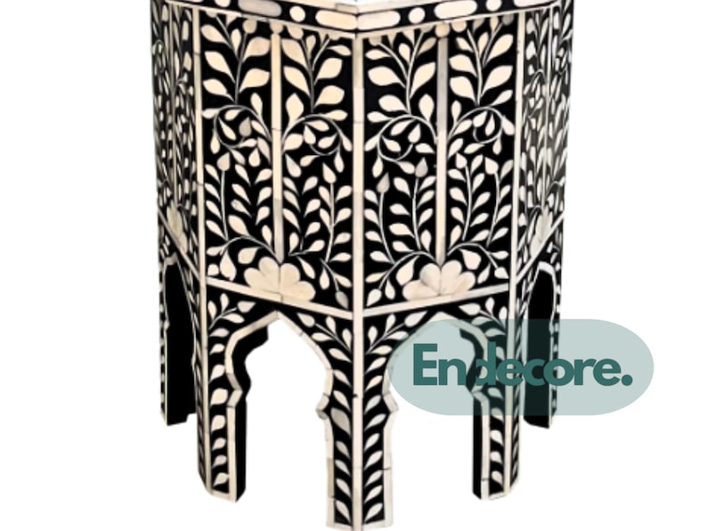 May include: A black and white hexagonal side table with a floral design. The table features a repeating pattern of white floral and leaf motifs against a black background. The table's legs have an arched design.