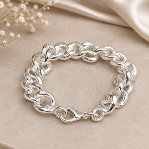 Peut inclure: Un bracelet à maillons en métal argenté poli composé de maillons épais et arrondis. Le bracelet est doté d'un fermoir mousqueton et comporte une petite étiquette rectangulaire près de la fermeture, présentant une finition métallique brillante.