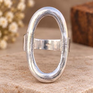 May include: A silver-toned ring featuring a large, vertically oriented oval-shaped band. The metal surface has a textured, slightly weathered appearance with a polished finish. The ring consists of a continuous, thick oval loop connected to a plain band.