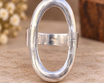 Könnte beinhalten: Ein silberfarbener Ring mit einem großen, vertikal ausgerichteten, ovalen Ringkopf. Die Metalloberfläche hat eine texturierte, leicht verwitterte Optik mit poliertem Finish. Der Ring besteht aus einer durchgehenden, dicken ovalen Schlaufe.