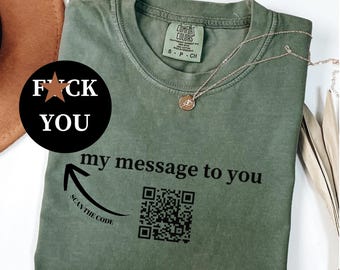 May include: Moss green Comfort Colors t-shirt with the text "FUCK YOU" in a black circle and "my message to you" with a QR code. A gold necklace is draped on the shirt.