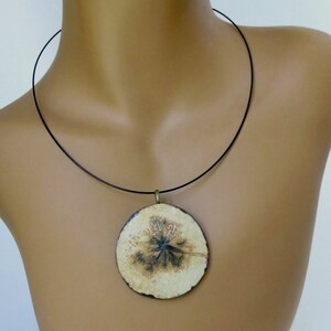 Puede incluir: Un collar con un colgante redondo de cer&aacute;mica blanca con un dise&ntilde;o floral negro. El colgante est&aacute; colgado de un cord&oacute;n negro.