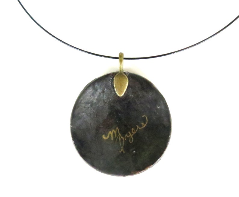 Puede incluir: Un collar con un colgante redondo negro, una anilla de metal dorado y una inscripci&oacute;n dorada que dice "M. Bryan".