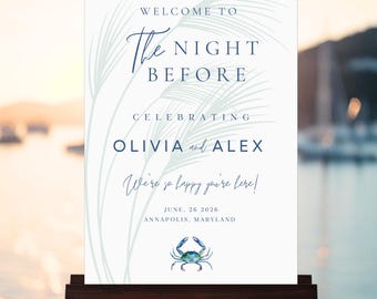 May include: A white wedding welcome sign on a wooden easel. The sign has navy blue text that reads "WELCOME TO The NIGHT BEFORE CELEBRATING OLIVIA and ALEX." A blue crab illustration is at the bottom. The date is June 26, 2026, Annapolis, Maryland.