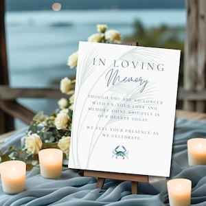 Puede incluir: Un letrero blanco sobre un pequeño caballete de madera con el texto "IN LOVING Memory". El letrero incluye una ilustración de cangrejo y el texto "THOUGH YOU ARE NO LONGER WITH US, YOUR LOVE AND MEMORY SHINE BRIGHTLY IN OUR HEARTS TODAY."