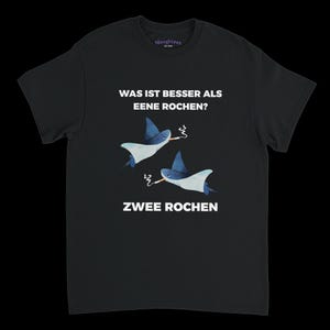 May include: A white ceramic mug with a black handle and the text "But First, Coffee" in a bold, black font. The mug is set against a blurred background, suggesting a cosy setting.