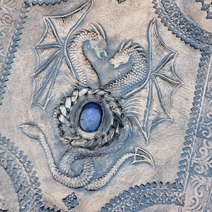 Luxury handcrafted leather ring binder journal with dragon motif, blue gemstone highlight and dramatic warm studio lighting