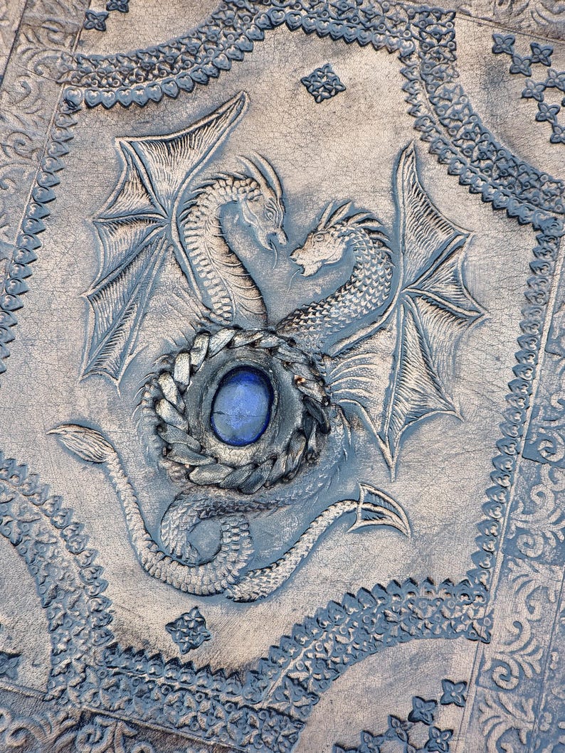 Luxury handcrafted leather ring binder journal with dragon motif, blue gemstone highlight and dramatic warm studio lighting
