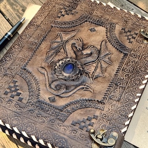 A4 leather ring binder journal with dragon embossing and blue gemstone detail, styled on parchment fabric and wooden background