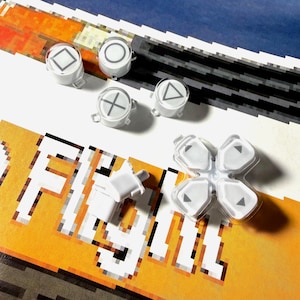 Może przedstawiać: Białe przyciski kontrolera PlayStation z szarymi symbolami, w tym kwadratem, okręgiem, trójkątem i krzyżem, są rozrzucone na pikselowanej pomarańczowo-białej powierzchni. Obecny jest również przezroczysty d-pad.