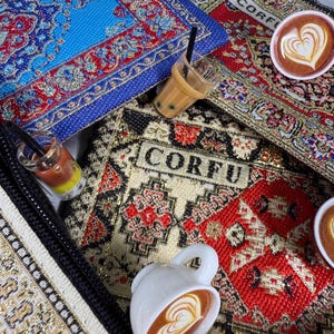 May include: Miniature scene featuring colorful, patterned rugs with the word "CORFU" visible. Small, detailed drinks include a bubble tea and coffee with latte art. A white coffee cup with a heart-shaped design is also present.