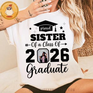May include: White t-shirt with the text "proud SISTER Of a Class Of - 2026 Graduate". The design includes a graduation cap, stars, and an image of a graduate. A perfect gift for a proud sister.