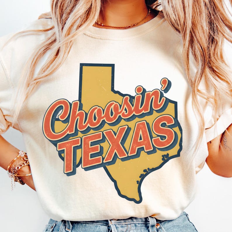 Puede incluir: Camiseta color crema con un gr&aacute;fico del estado de Texas en amarillo y las palabras "Choosin' TEXAS" en letras rojas y azules. El dise&ntilde;o tiene un aspecto vintage y desgastado.