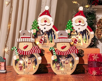 May include: Wooden Christmas decorations featuring Santa Claus and snowman designs. The Santa figures hold green Christmas trees. The snowman figures have red and white striped scarves and candy canes. The names "William", "Joseph", and "Sophia" are engraved on the decorations.