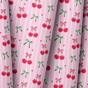 Puede incluir: Tela rosa con un patrón repetido de cerezas rojas atadas con lazos rojos y lazos verdes. El fondo tiene rayas blancas verticales y pequeñas estrellas rojas. La tela está doblada, mostrando profundidad y textura.