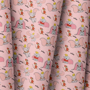 May include: Pink fabric featuring a repeating pattern of Dumbo the elephant and Timothy Q. Mouse from the Disney film. The design includes Dumbo in various poses, with the word "Dumbo" printed in black.