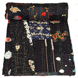 Puede incluir: Un edredón patchwork negro con bordados y costuras florales de colores. El edredón presenta varios cuadrados de tela con flores bordadas, hojas y otros elementos decorativos. El edredón está enrollado en la parte superior.