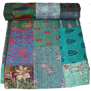 Può includere: Una trapunta patchwork con una varietà di colori e motivi. La trapunta presenta quadrati di tessuto verde acqua, verde e blu con disegni floreali e paisley. La trapunta è arrotolata nella parte superiore, mostrando i diversi tessuti.