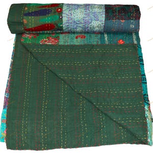 May include: A rolled-up, patchwork quilt with a dark green base and a variety of colorful, patterned squares. The quilt features red, blue, and teal accents, with visible stitching throughout. The quilt is made of soft fabric.