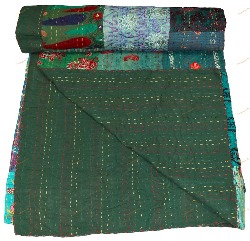May include: A rolled-up, patchwork quilt with a dark green base and a variety of colorful, patterned squares. The quilt features red, blue, and teal accents, with visible stitching throughout. The quilt is made of soft fabric.