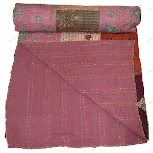May include: A patchwork quilt in shades of mauve, rust, and burgundy, with intricate embroidered details and mirror accents. The quilt is folded, revealing a contrasting solid mauve underside and gold stitching.