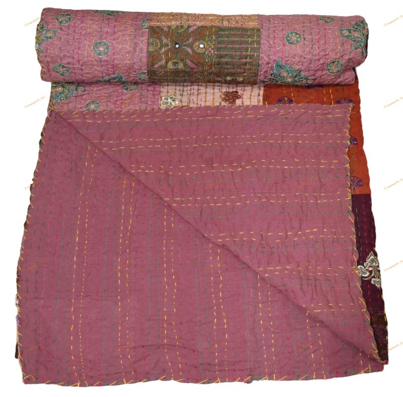 May include: A patchwork quilt in shades of mauve, rust, and burgundy, with intricate embroidered details and mirror accents. The quilt is folded, revealing a contrasting solid mauve underside and gold stitching.
