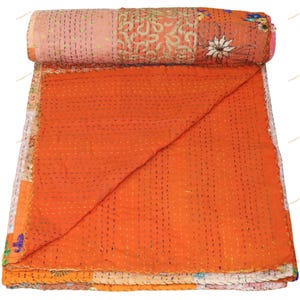 May include: A rolled-up, handmade quilt with a patchwork design. The quilt features a vibrant orange center, with sections of pink, white, and patterned fabric. The quilt is hand-stitched with visible thread and has a floral design.