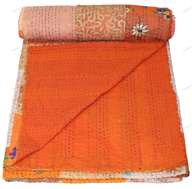 May include: A rolled-up, handmade quilt with a patchwork design. The quilt features a vibrant orange center, with sections of pink, white, and patterned fabric. The quilt is hand-stitched with visible thread and has a floral design.