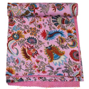 Può includere: Una trapunta floreale rosa con una sezione arrotolata. La trapunta presenta un motivo ripetuto di fiori colorati, foglie e altri elementi botanici nelle tonalità del rosso, blu, giallo e verde. La trapunta è realizzata in un tessuto morbido e leggero.